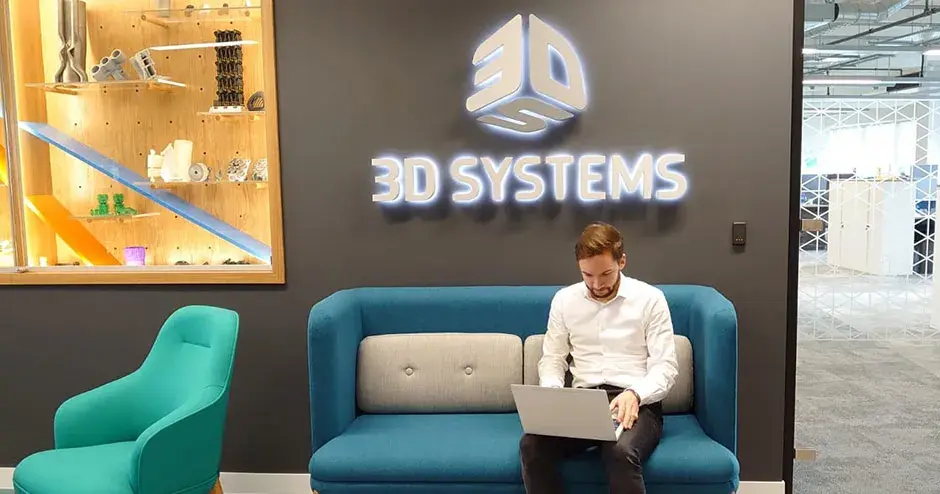 Um homem sentado em uma sala da 3D Systems e trabalhando em seu laptop