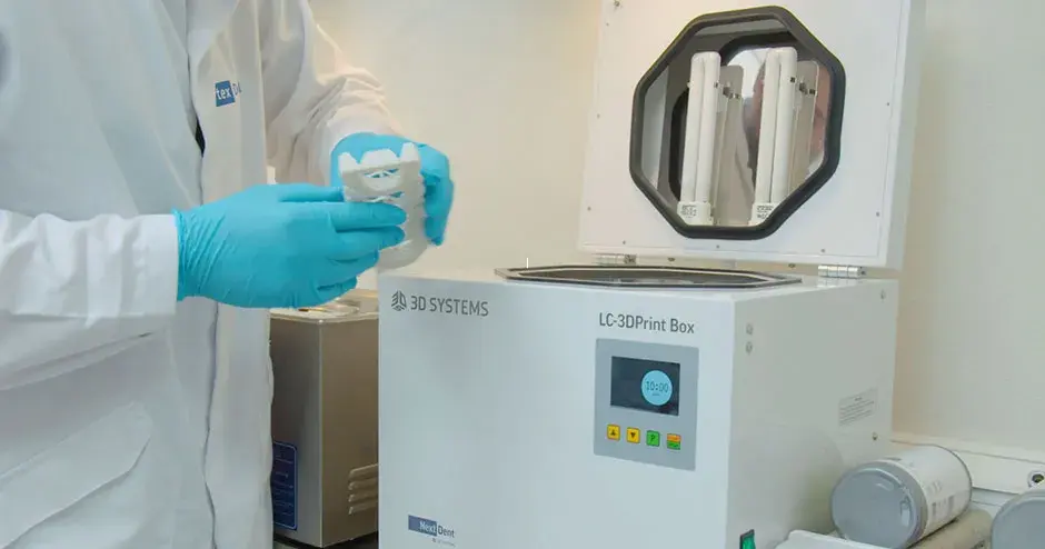 uma pessoa segurando uma prótese retirada de uma máquina de pós-processamento