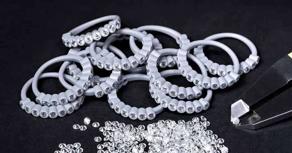 muitos anéis moldados de cera cravejados de diamantes, pinça segurando um diamante, diamantes espalhados