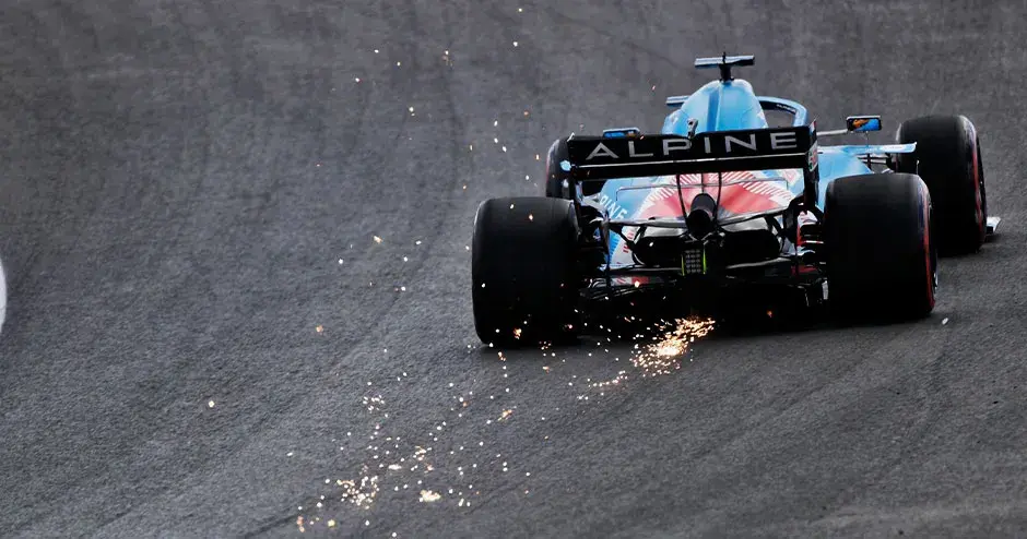 carro de corrida da alpine f1 na pista sendo dirigido com faíscas saindo da parte traseira do carro